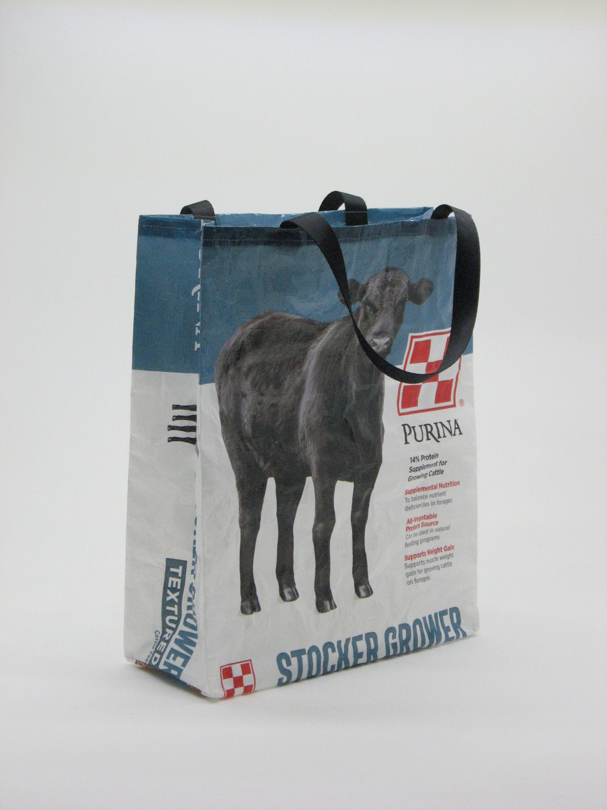 A reusable fabric shopping tote bag with black handles, featuring a printed design of a horse on a blue and white background with text including 'PURNA' and 'STOCKED BREEDER'.