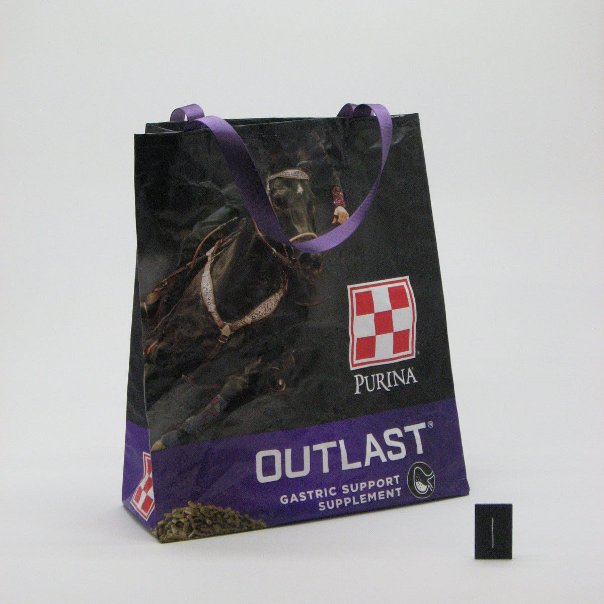 A Purina Outlast Gastric Support Supplement bag, featuring a black and purple design with a horse graphic, purple handles, and a small black scale marker on a white background.