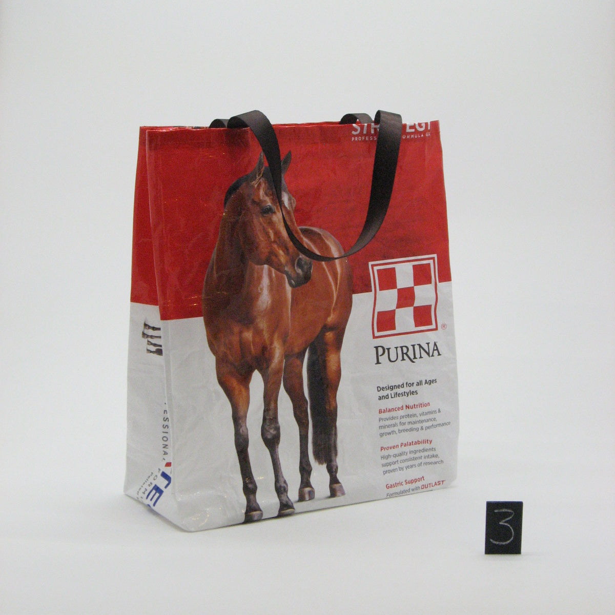 A printed Purina reusable shopping bag with a red and white design featuring a horse graphic, photographed against a plain white wall.